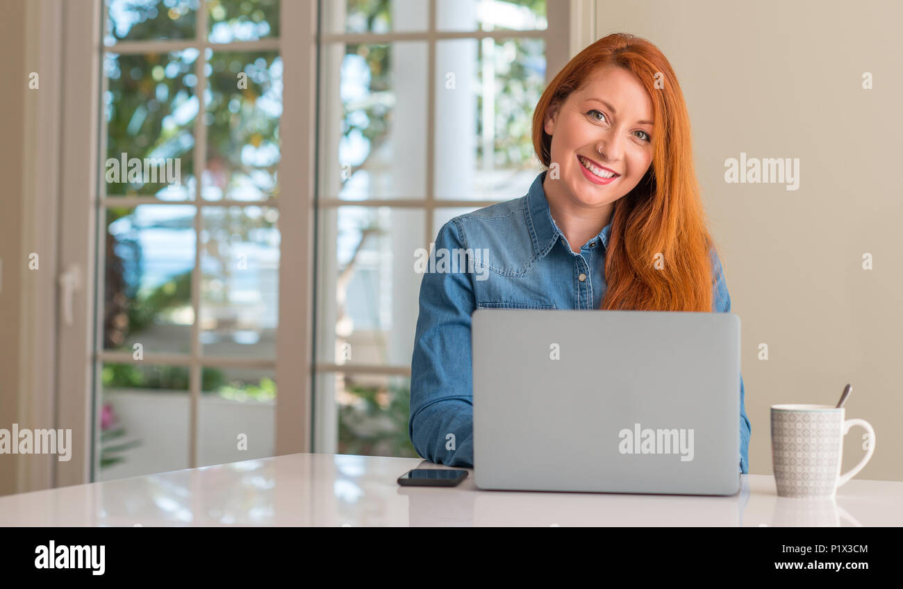 Redhead woman using computer laptop at home with a happy face standing ...