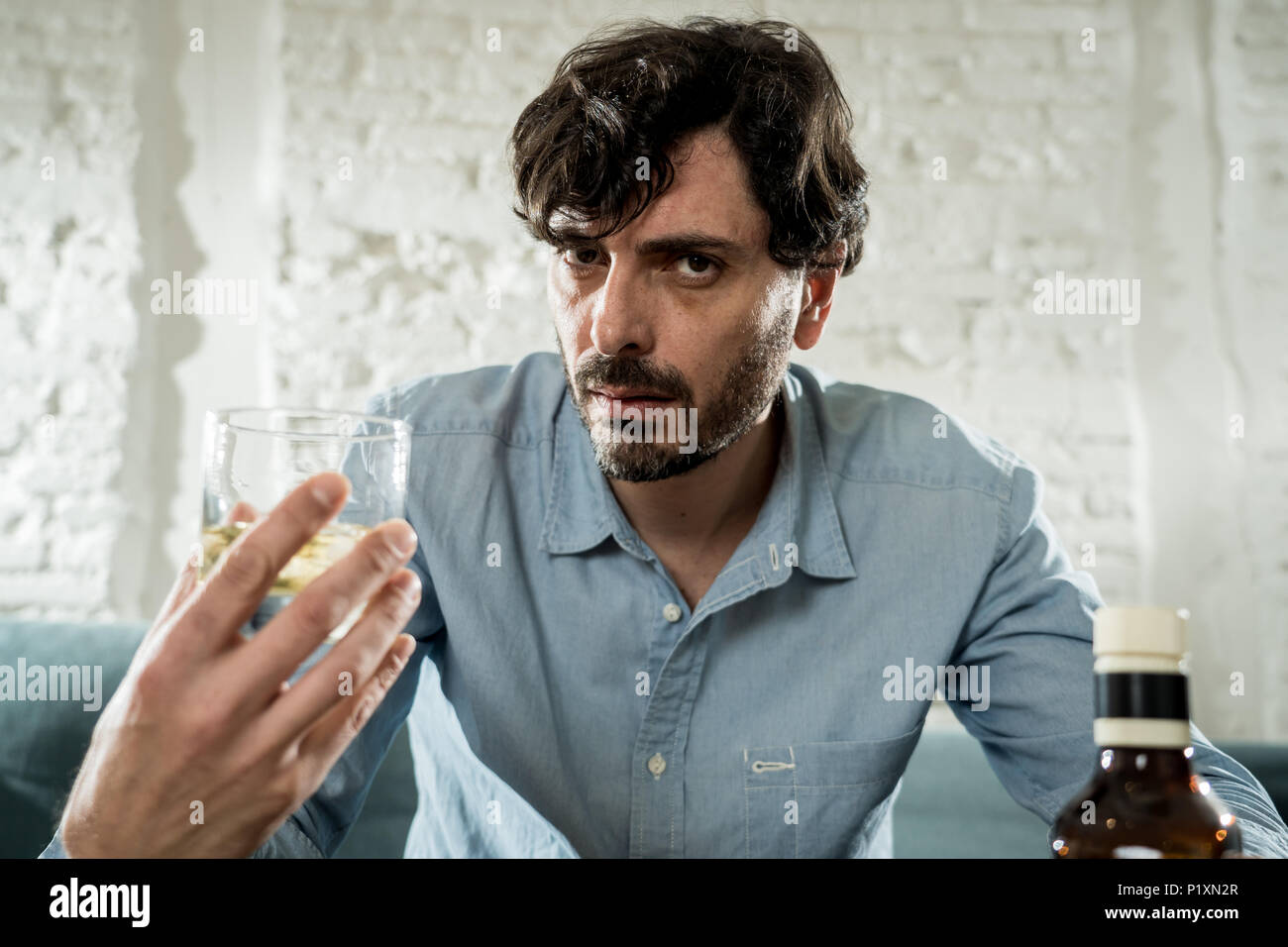 drunk alcoholic lain business man drinking whiskey from the bottle and glass depressed wasted and sad at home couch in alcohol abuse and alcoholism co Stock Photo