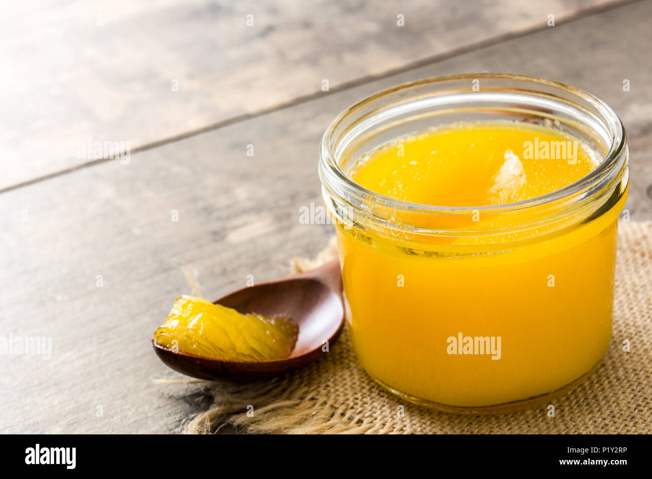 Ghee or clarified butter in jar and wooden spoon on wooden table