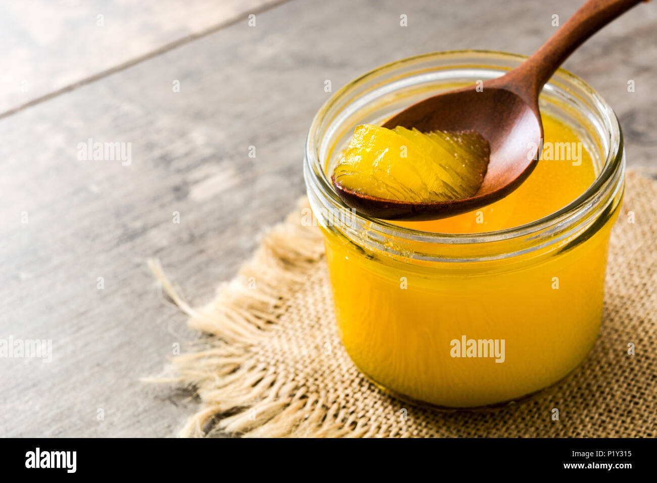Ghee or clarified butter in jar and wooden spoon on wooden table