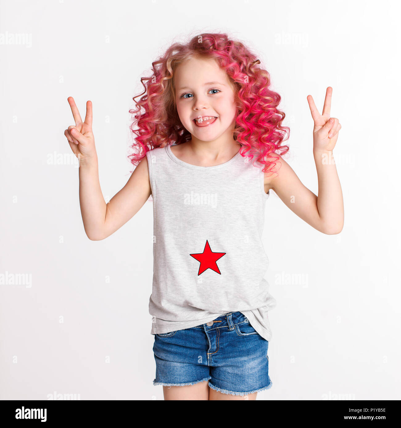 Colored wavy hairs. Little modern hipster girl in fashion clothes, make peace by her hand. Studio. Isolated on white Stock Photo