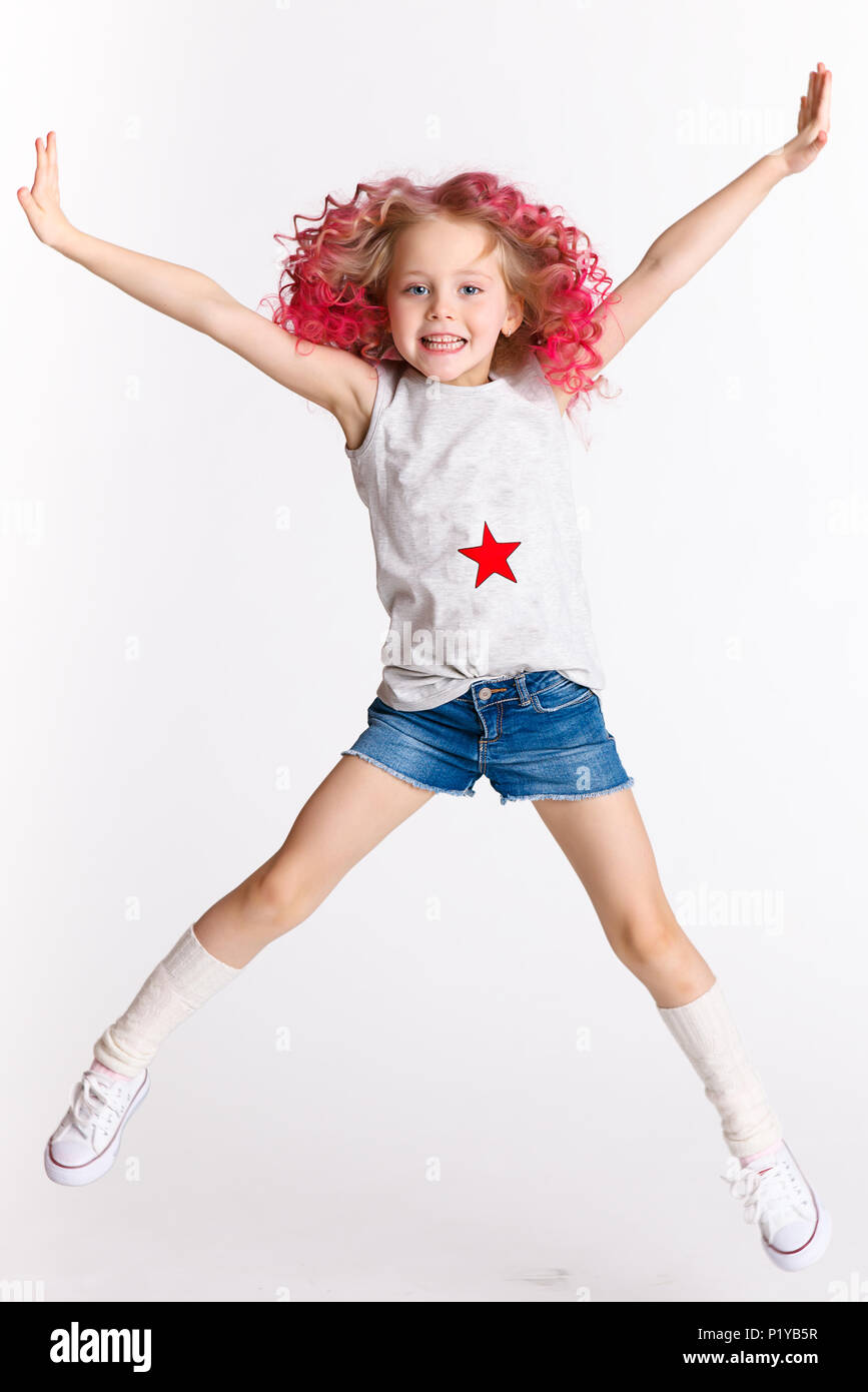 Colored wavy hairs. Little modern hipster girl in fashion clothes, jumping in studio. Isolated on white Stock Photo