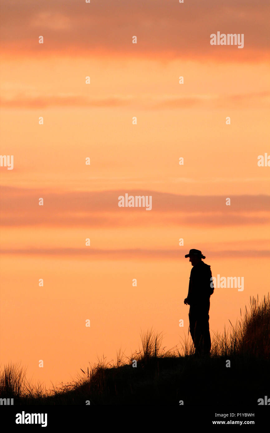 Normandy. Manche. Montmartin sur Mer. Man wearing a cowboy hat watching the sunset. Stock Photo