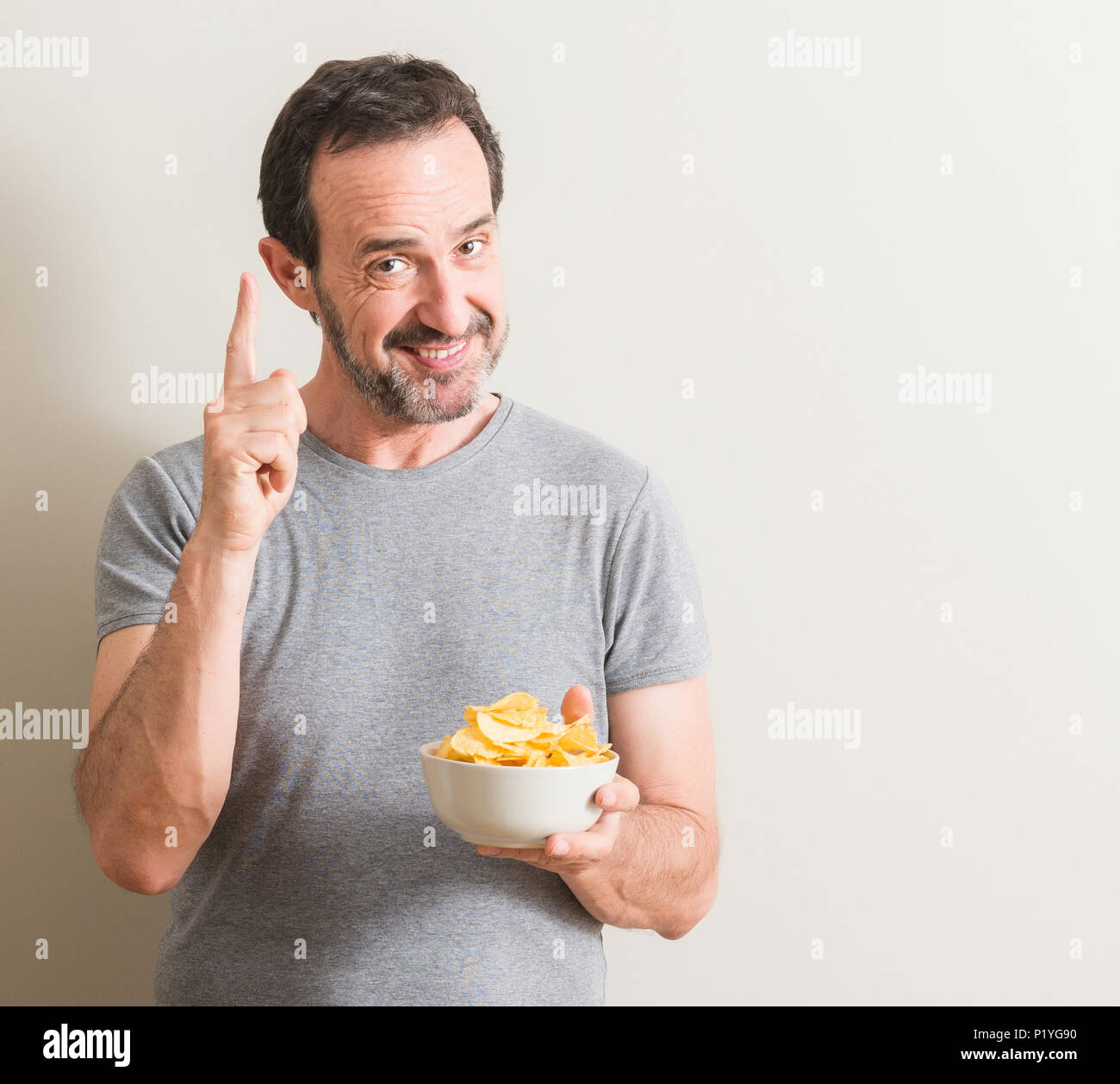 Senior man eating potato chips surprised with an idea or question