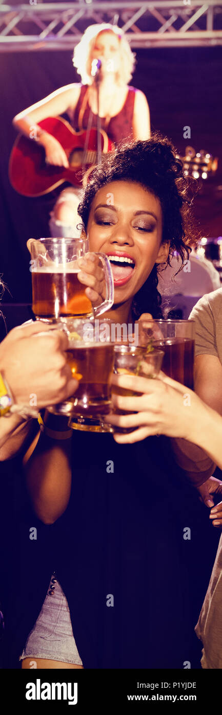Friends toasting beer glasses with performer in background Stock Photo