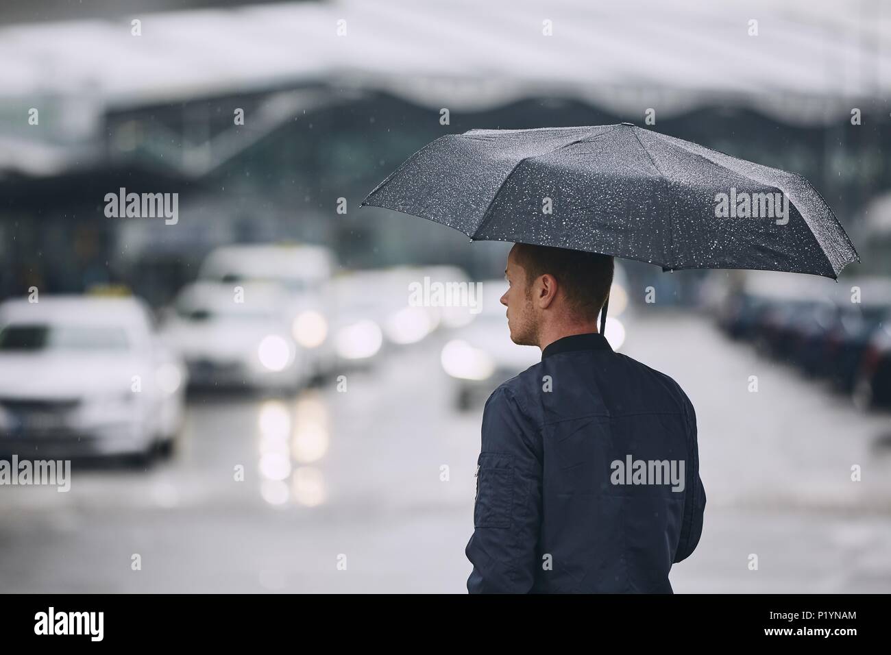 Rain in city. Young man holding umbrella walking in the street. Stock Photo