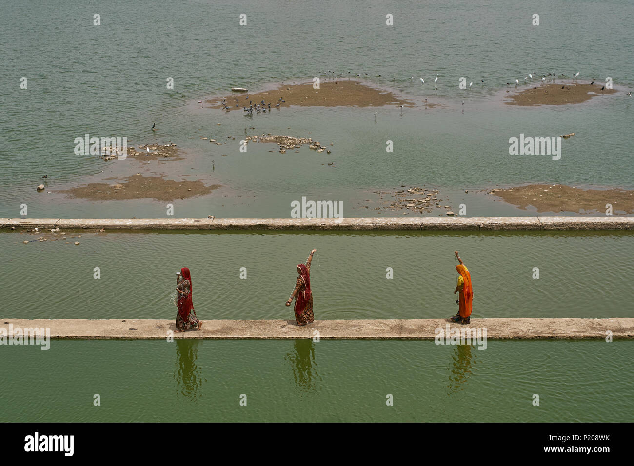 Three Indian women walking on a stone bridge over water while preforming a ritual. Stock Photo