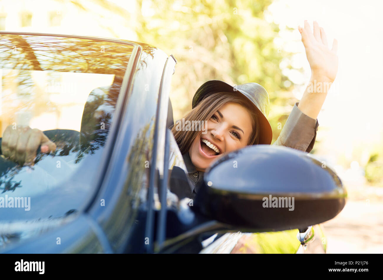 Shot of a young cute woman enjoying a drive in a convertible loving the breeze in her face waving with her arm Stock Photo