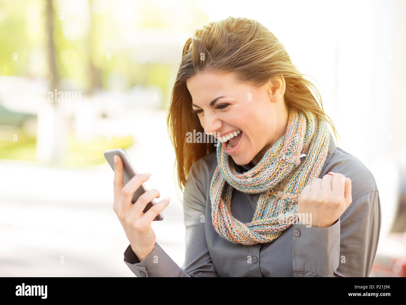 Excited student reading good news on line on mobile phone outdoors on a summer day with sunlit street background Stock Photo