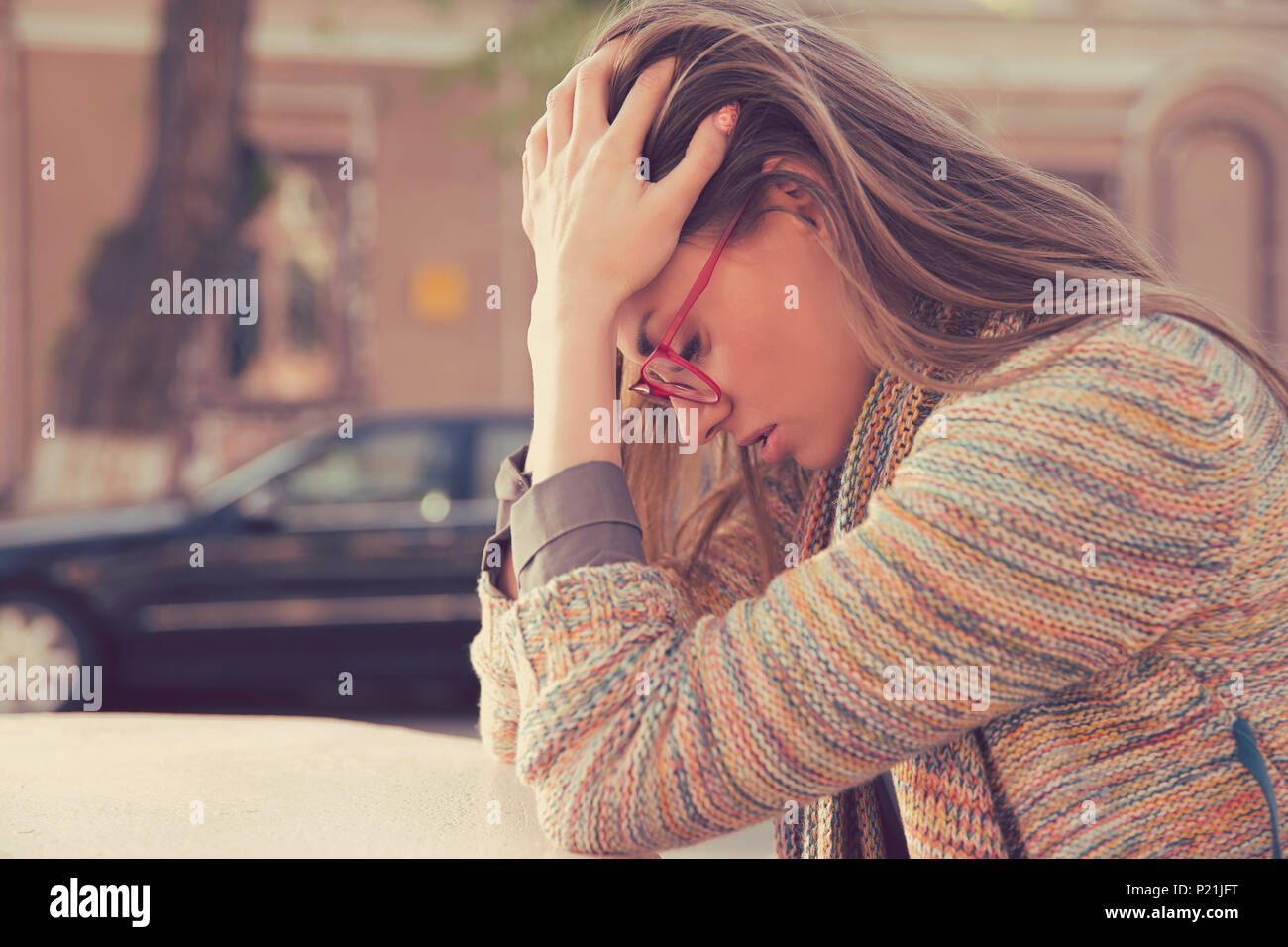 Side profile stressed sad young woman sitting outdoors with broken down car on background. City urban life style stress Stock Photo