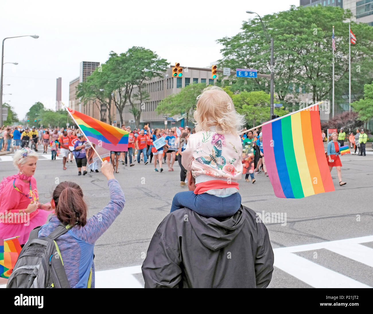 Young girl on dad's shoulders waves a rainbow flag, alongside her mom, as the 2018 Pride parade makes its way through downtown Cleveland, Ohio, USA. Stock Photo