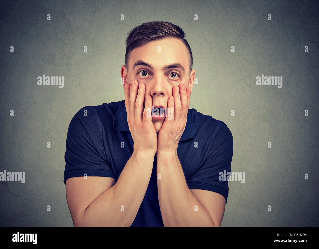 Young casual man touching face in despair posing on gray and looking at camera with fear. Stock Photo