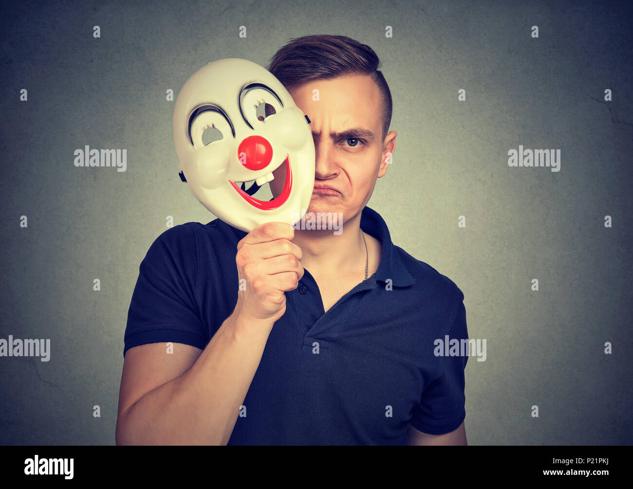 A little mad. Young negative man hiding real face with clown mask having split personality. Stock Photo