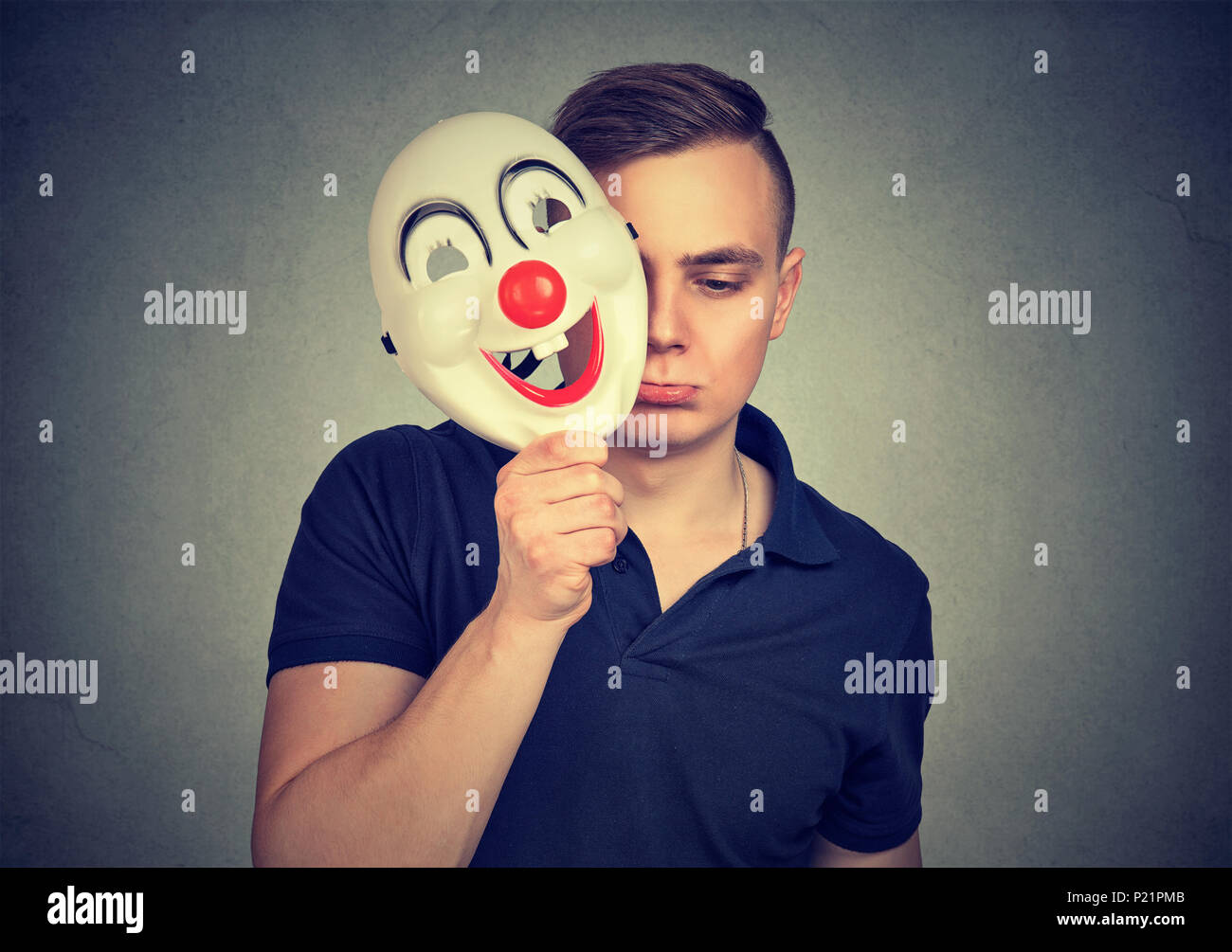 Sad and depressed man covering face with happy clown mask hiding his personality. Stock Photo