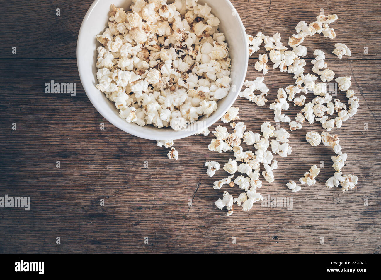 directly above shot of bowl filled with popcorn and spilled popcorn on rustic wooden table Stock Photo