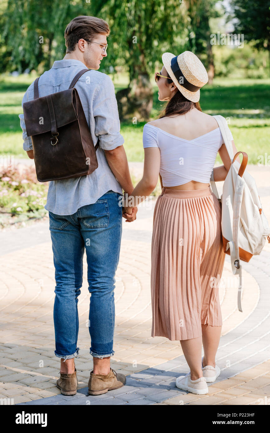 back view of multicultural couple holding hands while walking in summer ...