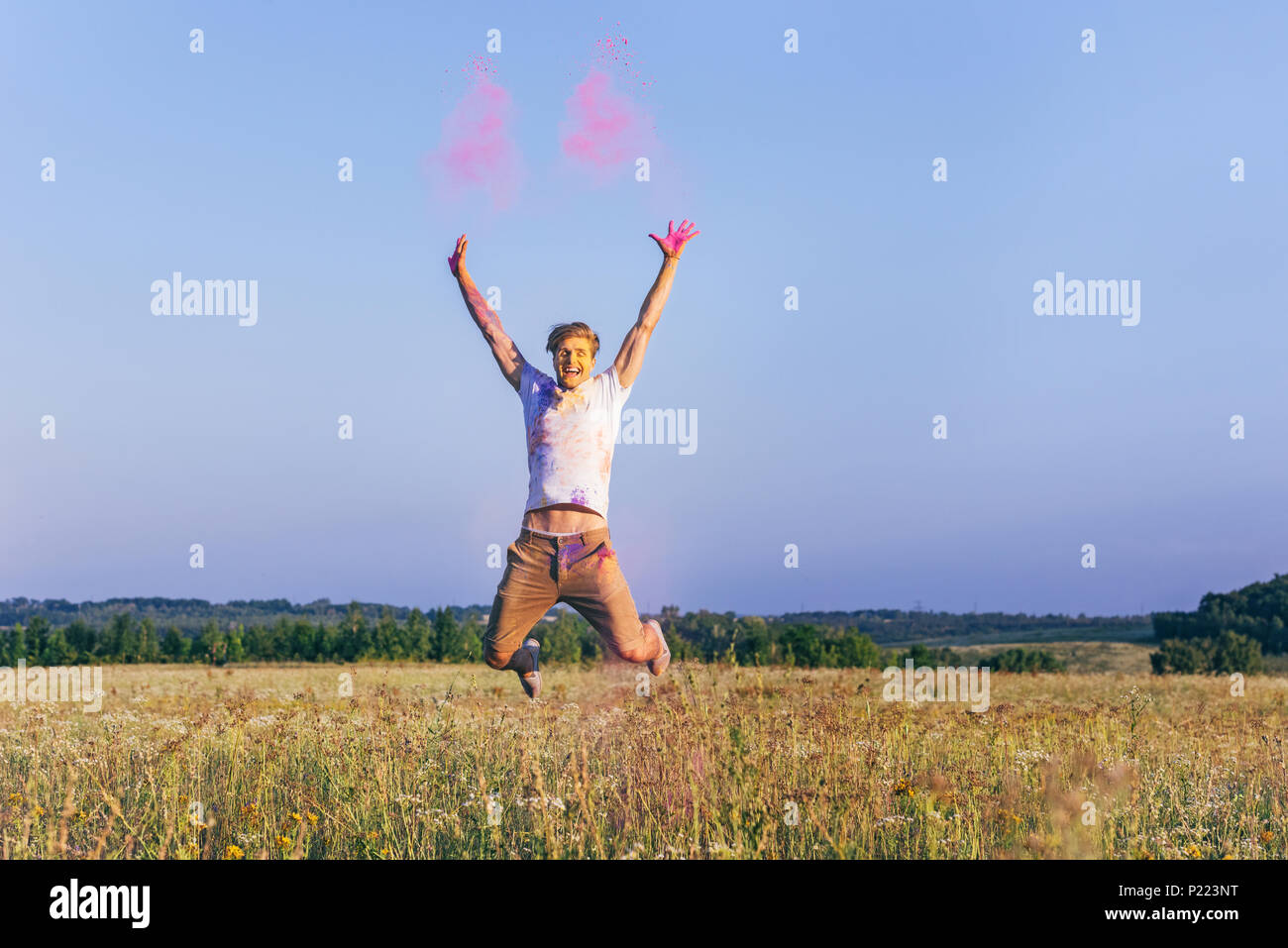happy caucasian man jumping in field during holi festival Stock Photo