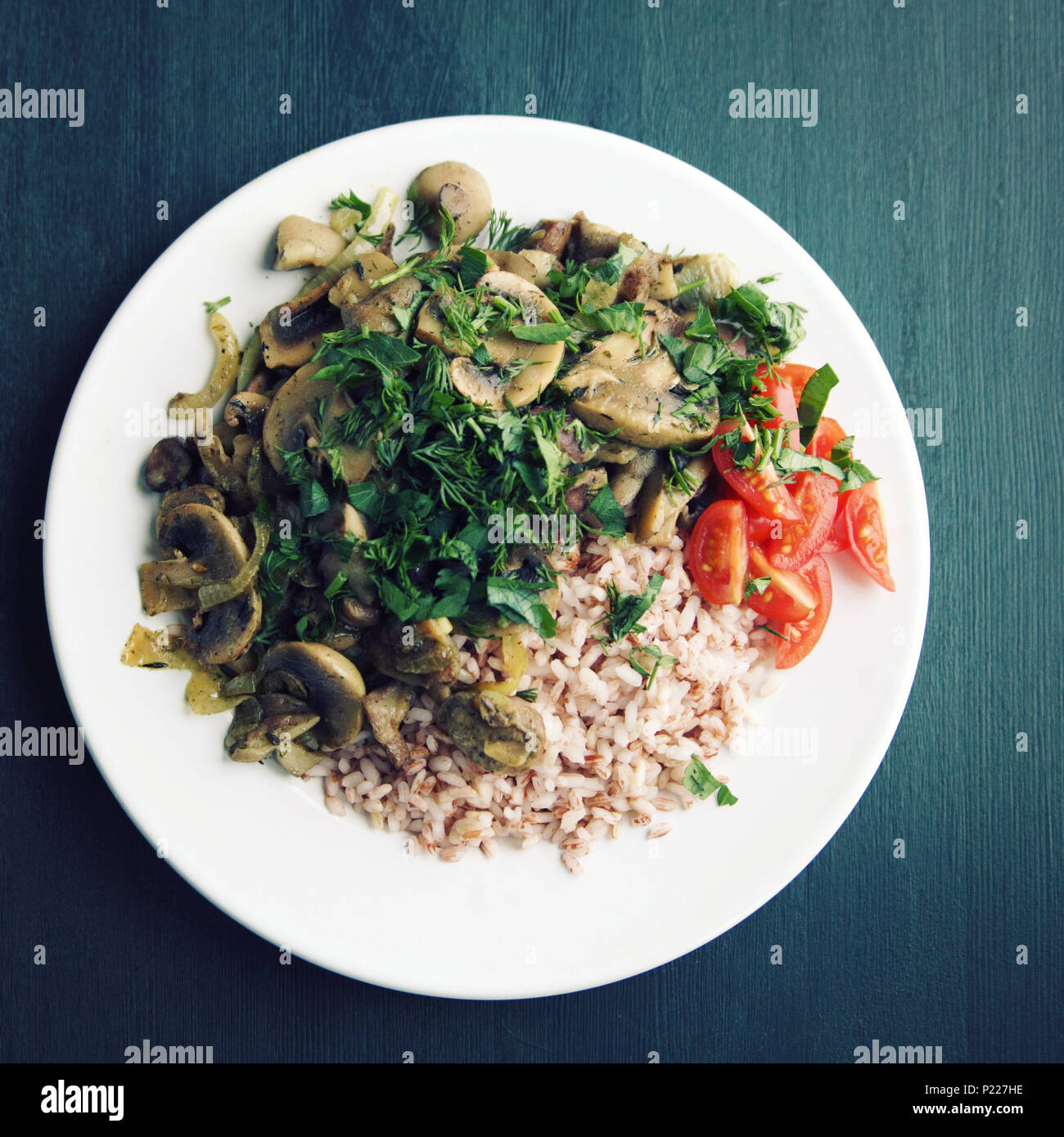 Red rice with mushrooms and cherry tomatoes. Vegan dish. European cuisine. Simple healthy lunch on the black background. Vegetarian rice dish on the w Stock Photo