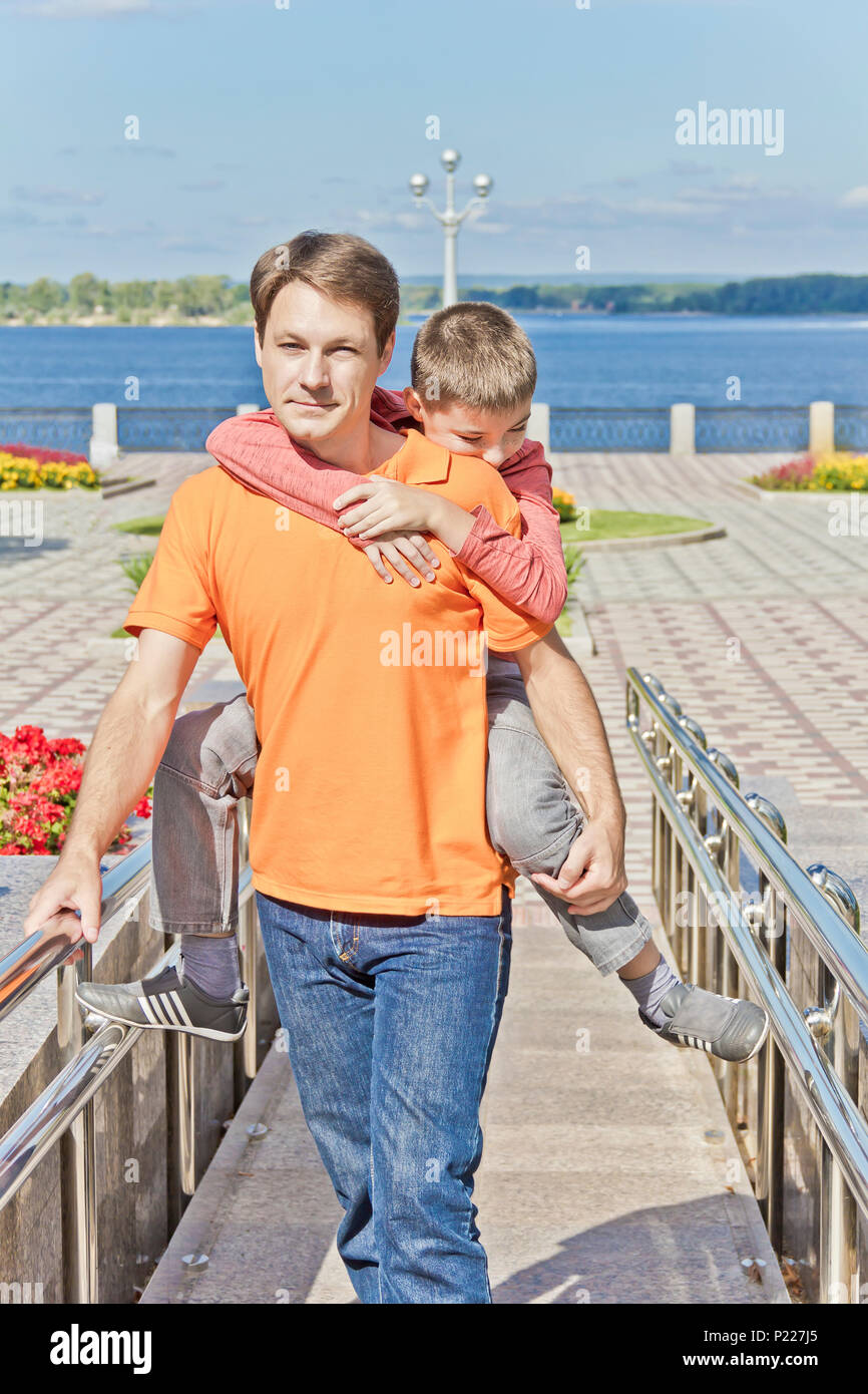 Son is hanging on father shoulders at embankment Stock Photo - Alamy