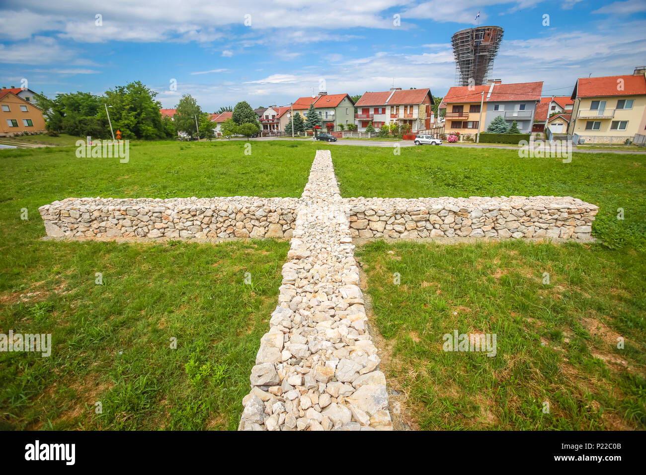 A view of the votive stone cross as a symbol of the sacrifice and suffering of the city during the Independence war with the Vukovar water tower in th Stock Photo