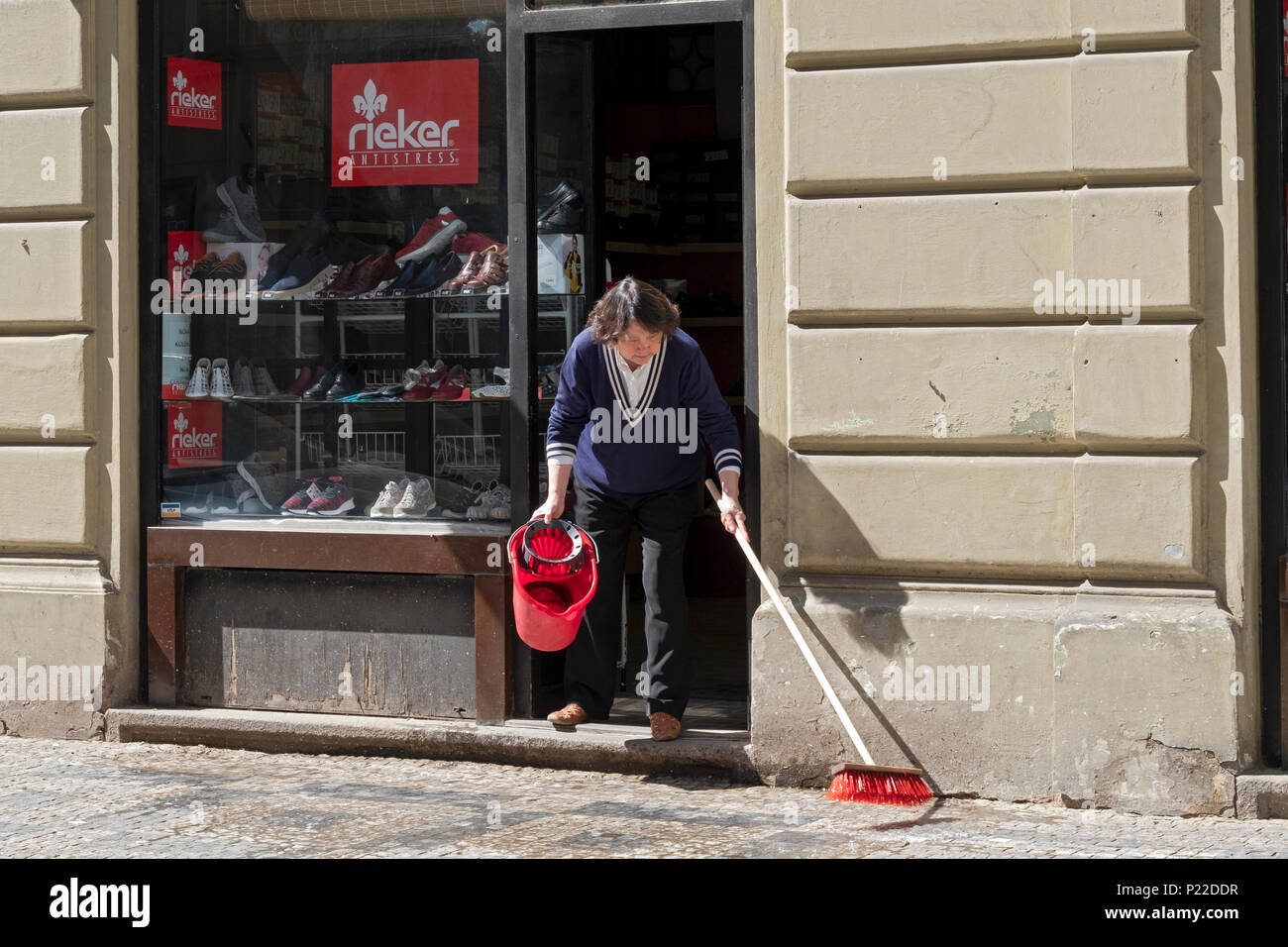 An Asian woman scrubbing the sidewalk outside of a shoe shop on Maiselova Street in Prague, Czech Republic. Stock Photo