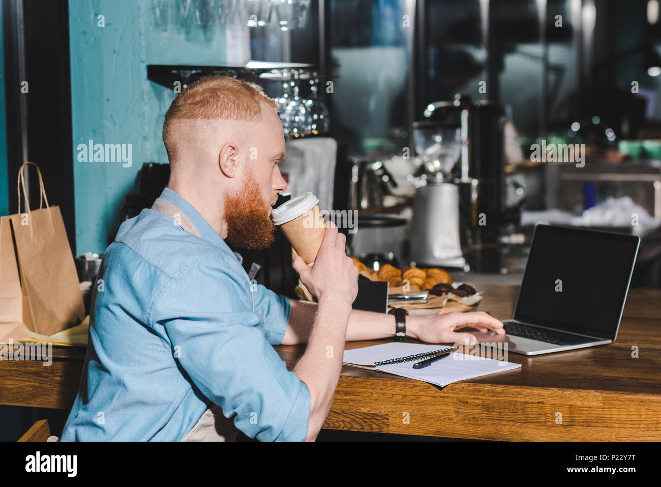 side view of young male barista drinking coffee from paper cup and ...