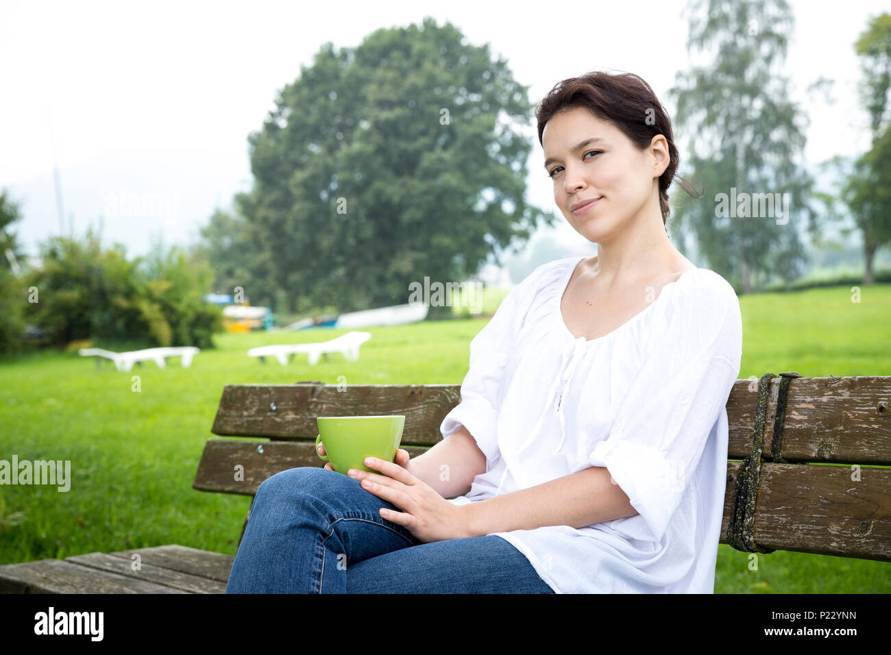 Young woman with a cup of tea sitting on a bench Stock Photo - Alamy