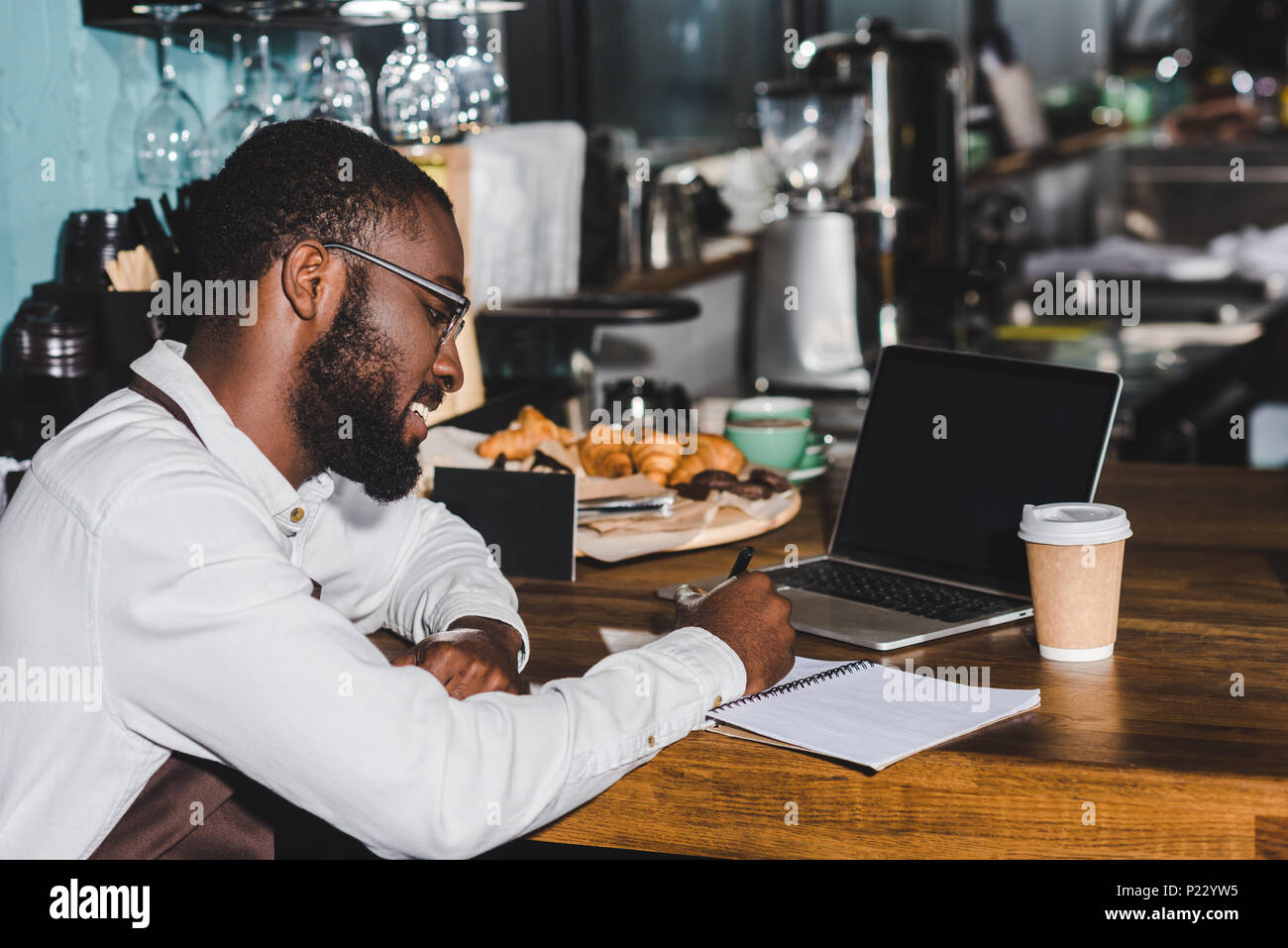 smiling young african american barista in eyeglasses taking notes and ...