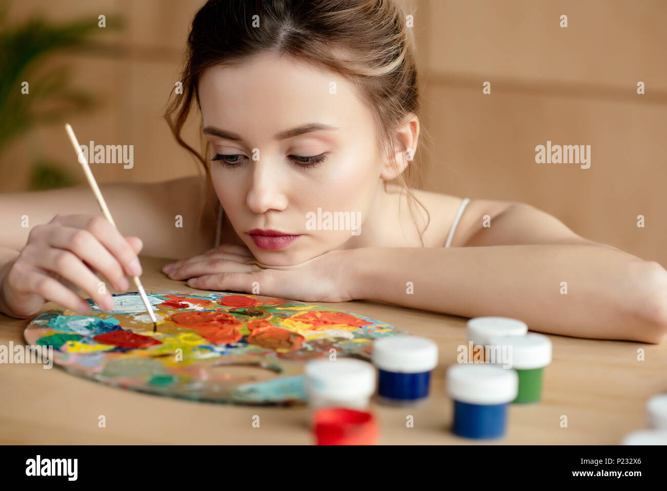 beautiful young artist holding brush and looking at palette in art ...