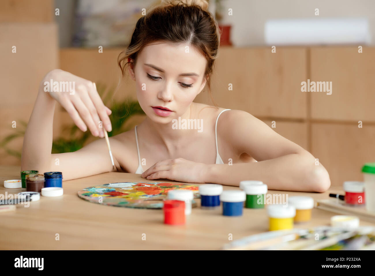 beautiful young female painter holding brush and looking at palette in ...