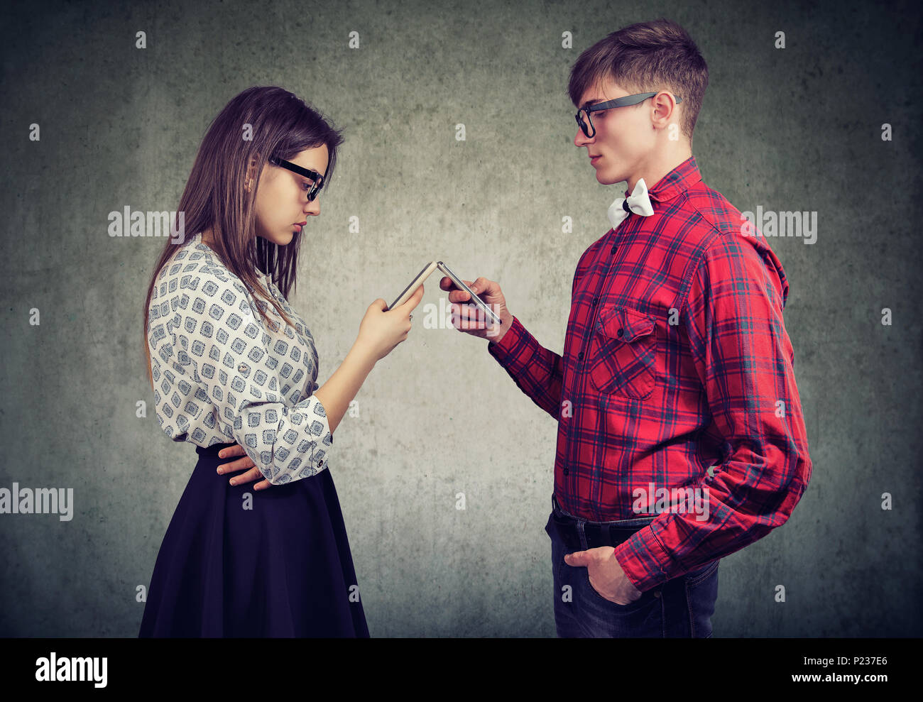 Stylish young couple using smartphones totally absorbed in online life, with obsessed look, not talking to each other, facing one another. Internet ad Stock Photo