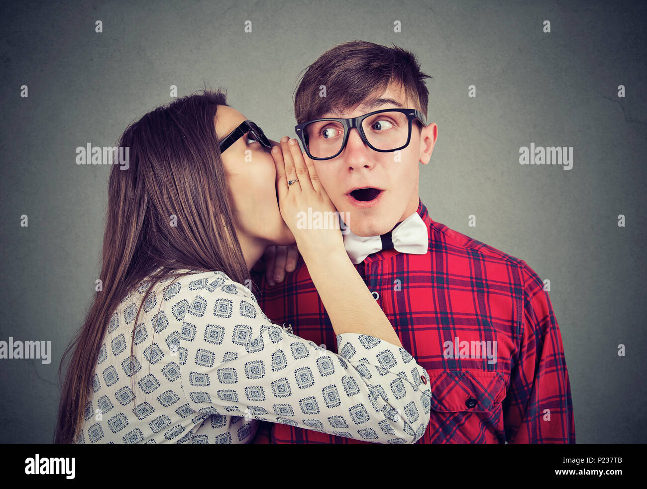 Young woman telling whispering secret gossip in the ear to an amazed shocked man with wide open mouth. Human emotions face expression reaction. Hot ne Stock Photo