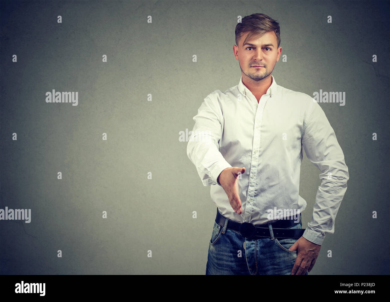 Confident young man outstretching hand for handshake when greeting partner on gray background. Stock Photo