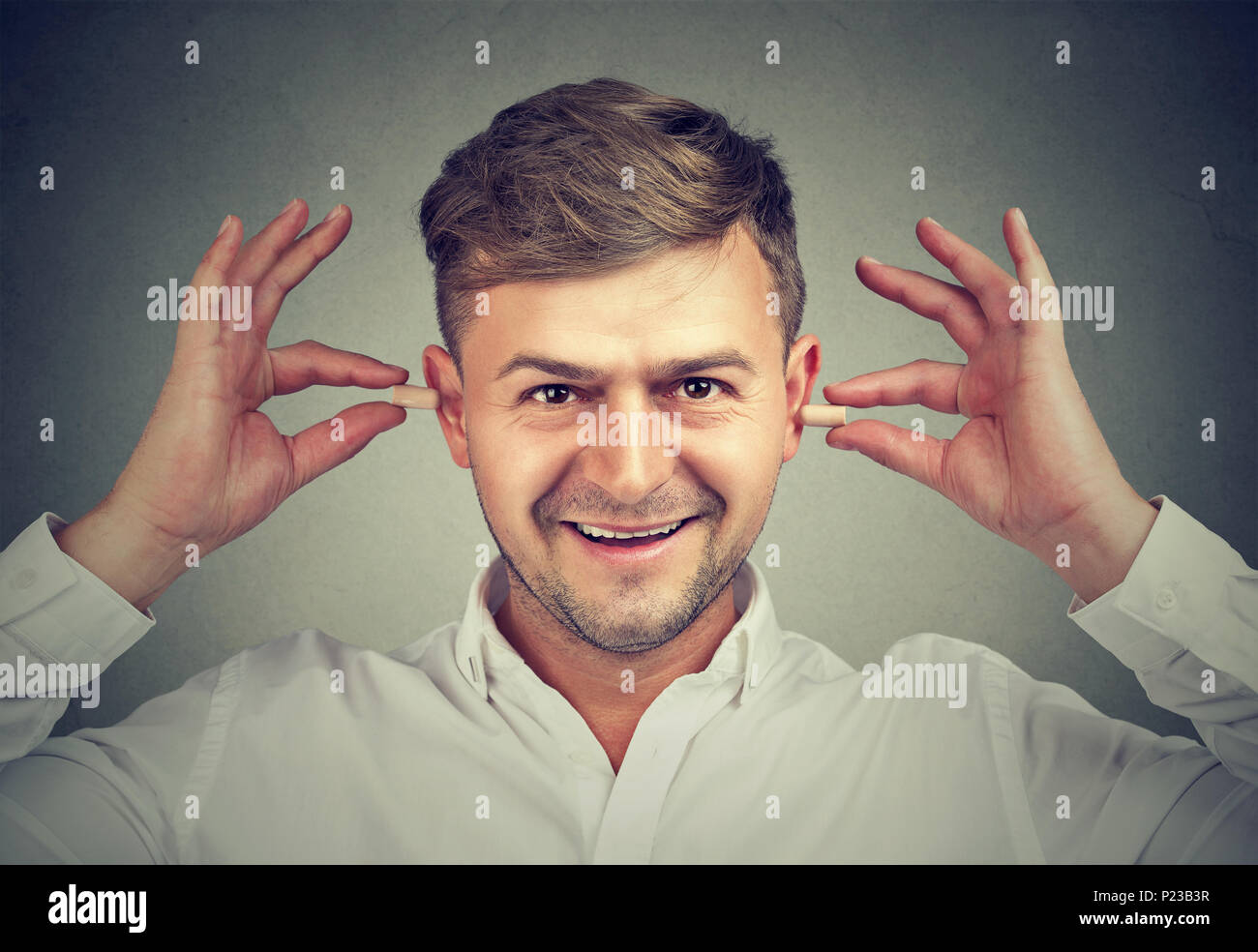 Content man inserting ear plugs happy with solution of loud neighbours problem looking at camera. Stock Photo