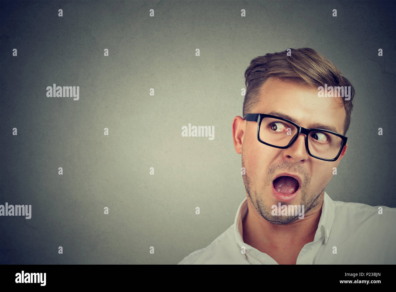 Young expressive guy in glasses with mouth opened listening carefully to gossips looking away in surprise. Stock Photo