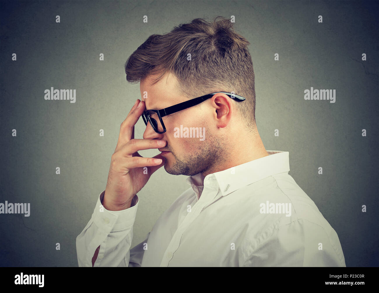 Young man in elegant shirt and glasses rubbing forehead and thinking in anxiety. Stock Photo