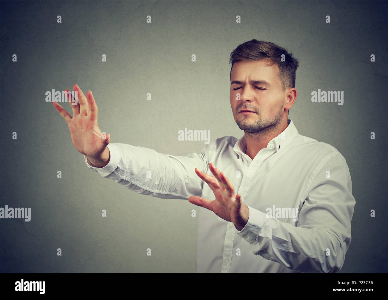 Young man with eyes closed pushing hands forward walking in darkness with help of intuition. Stock Photo