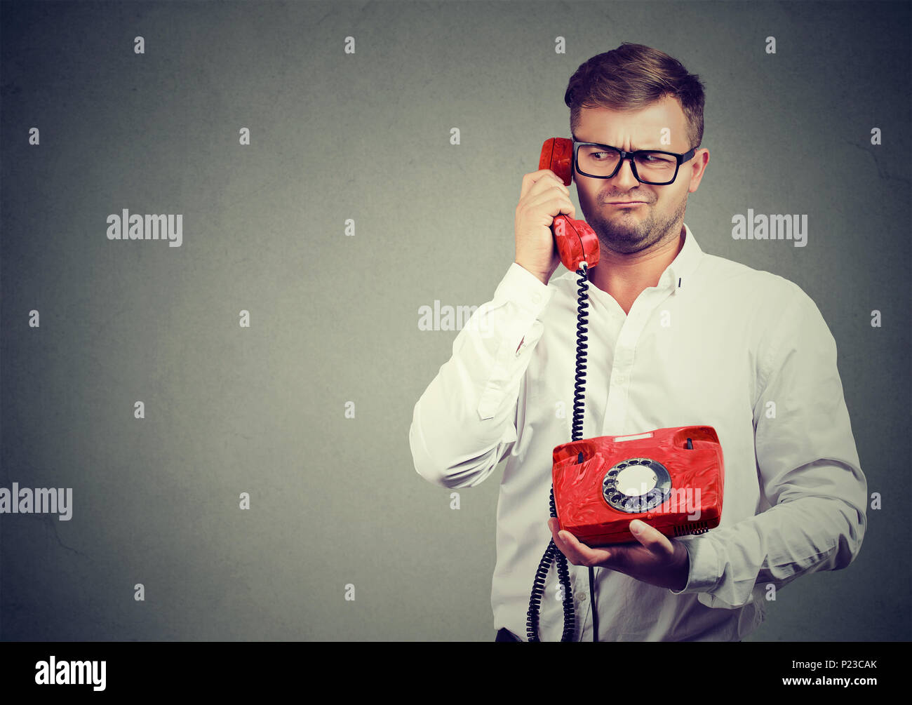 Casual man in eyeglasses talking on old-fashioned phone looking away in misunderstanding. Stock Photo