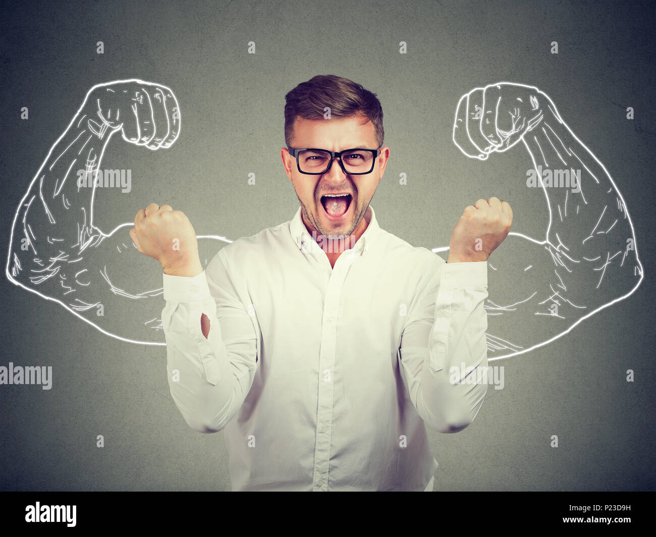 Young man holding fists up shouting with determination at camera on background of painted strong arms. Stock Photo
