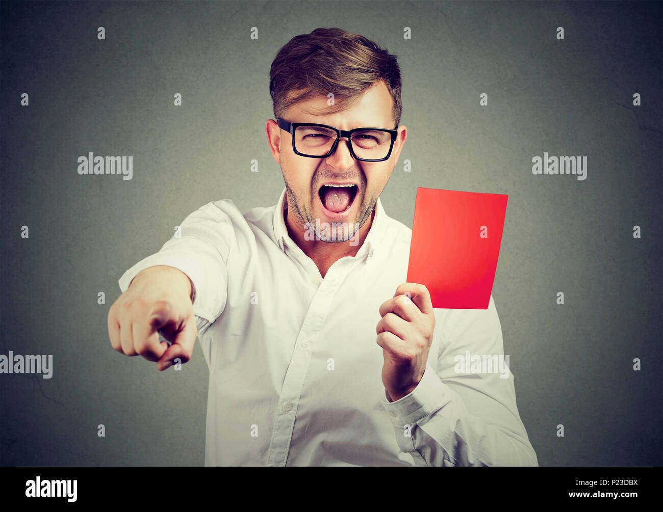 Expressive young man in eyeglasses shouting and pointing at camera giving red card. Stock Photo