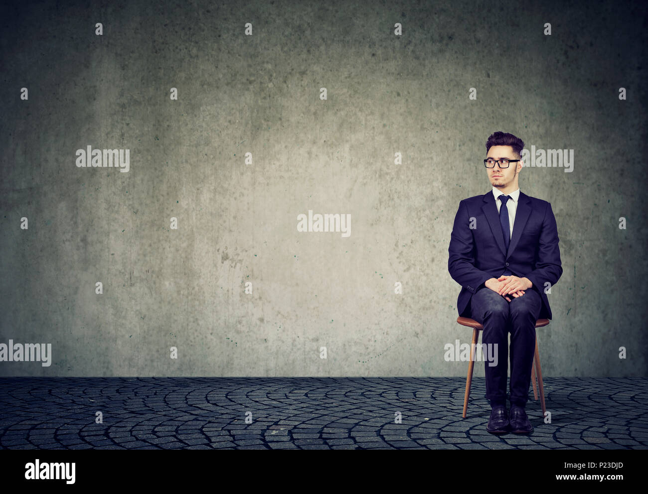 Nervous young man in suit sitting on chair expecting interview session in anxiety. Stock Photo