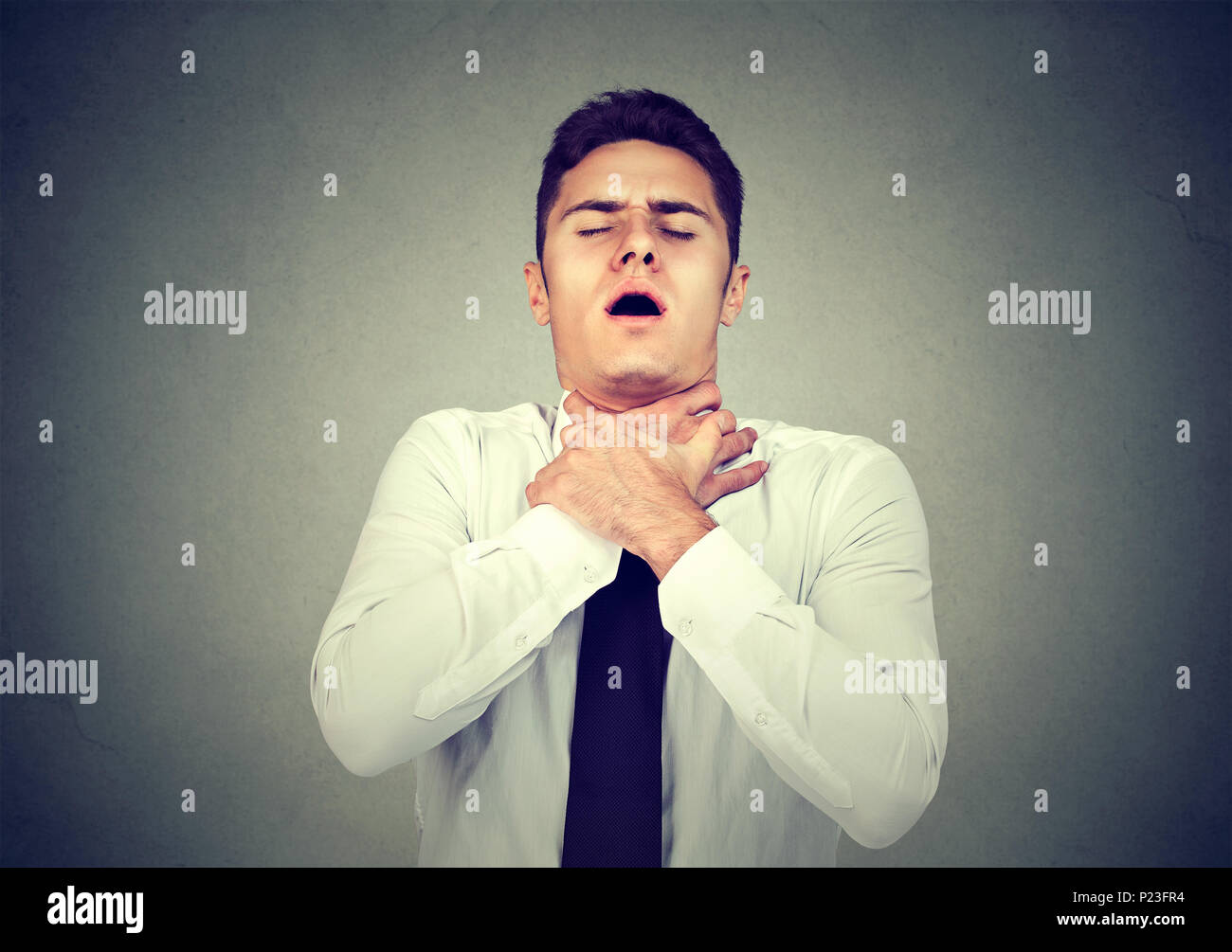 Young man having asthma attack or choking can't breath suffering from respiration problems isolated on gray background Stock Photo