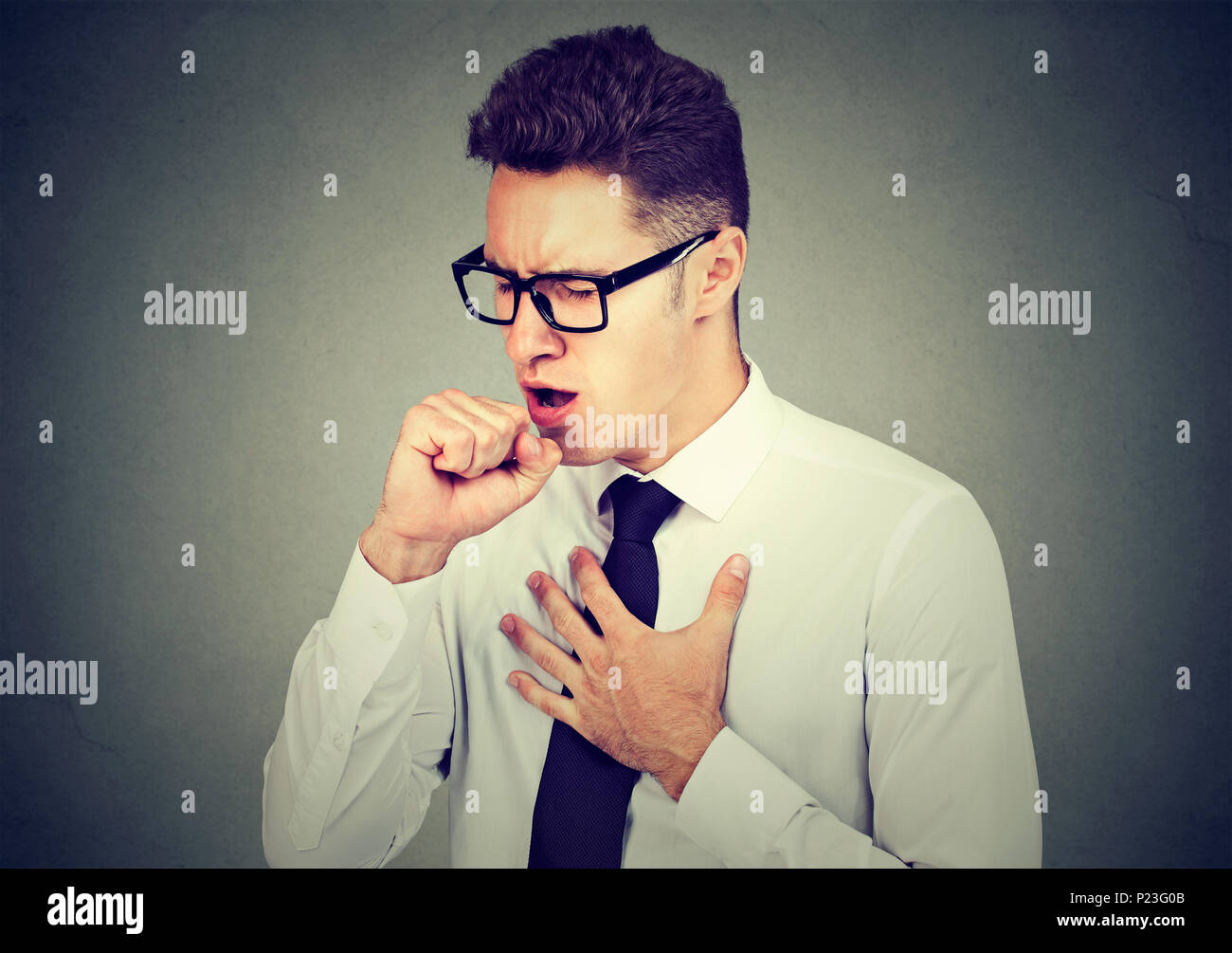 Young sick man coughing with post nasal drip holding fist to mouth Stock Photo