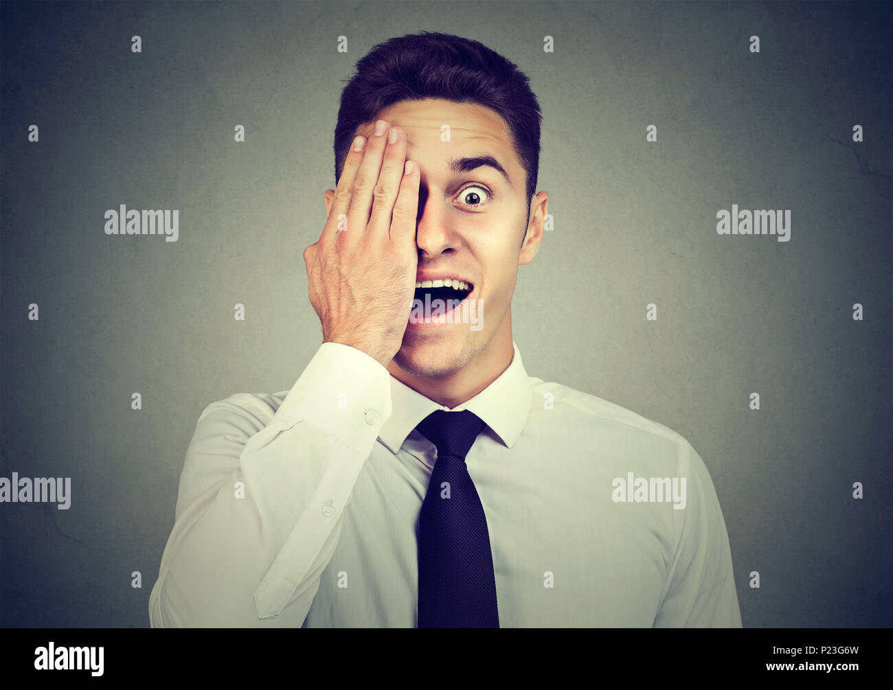 Surprised business man covering his eye with hand isolated on gray wall ...