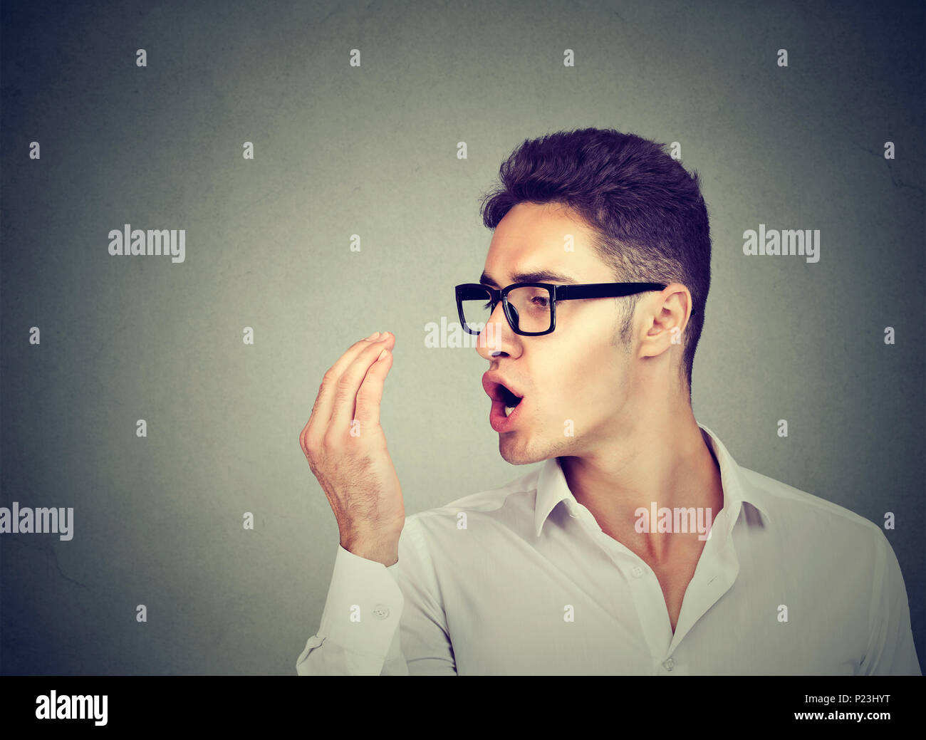 Young man in glasses checking his breath with hand. Stock Photo