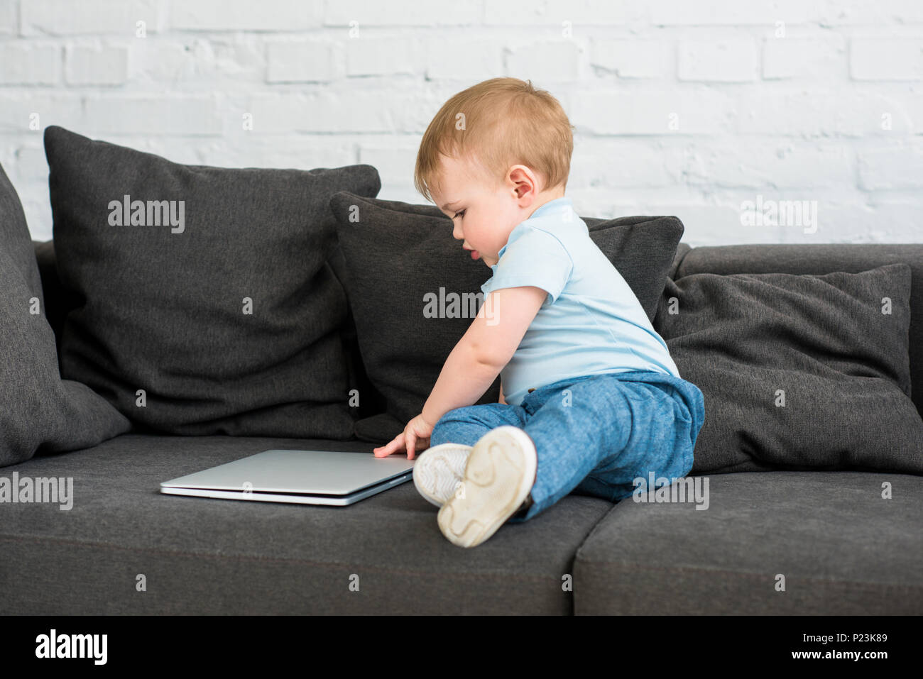 side view of little baby boy with laptop on sofa at home Stock Photo ...
