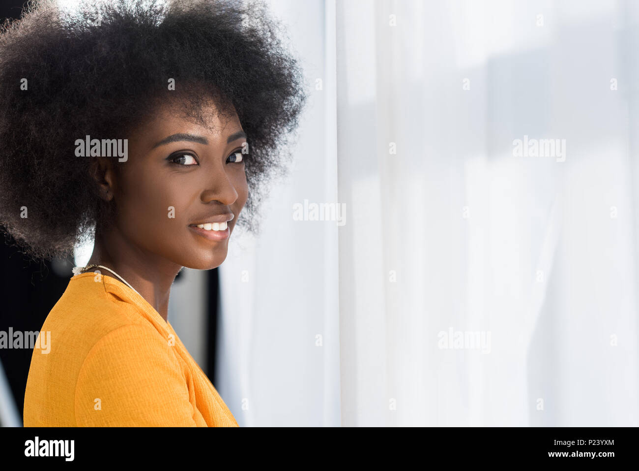 side view of smiling african american woman looking at camera at home ...