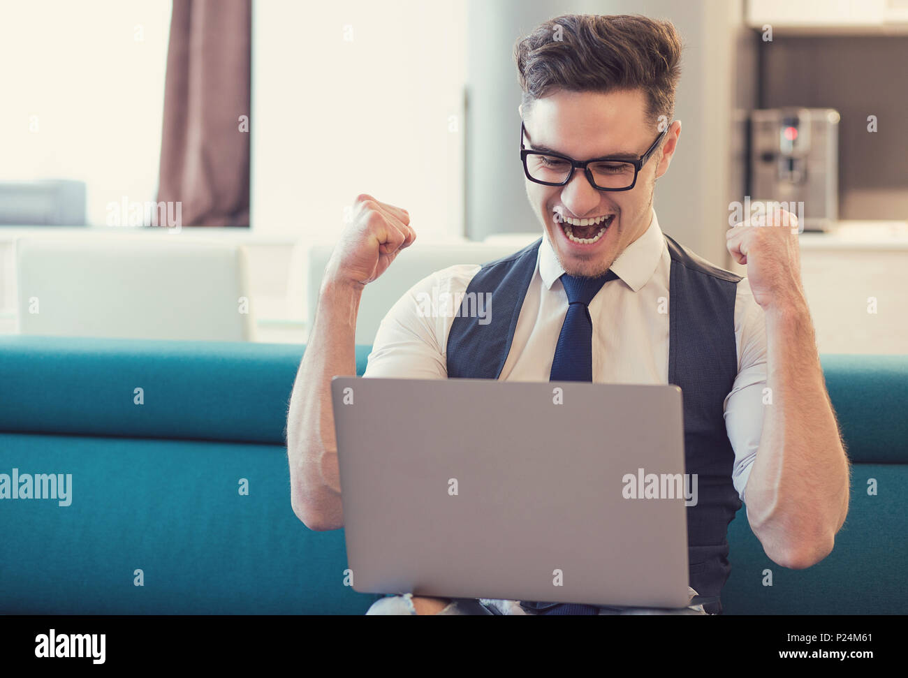 Young man using laptop and celebrating good news looking happy while sitting on couch. Stock Photo