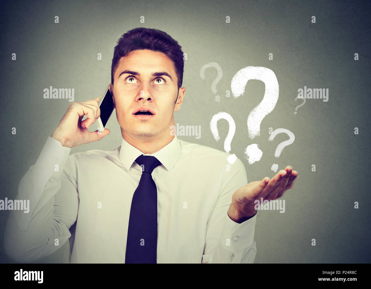 Misunderstanding and distant call concept. Upset annoyed young man talking on mobile phone has many questions isolated on gray background. Stock Photo