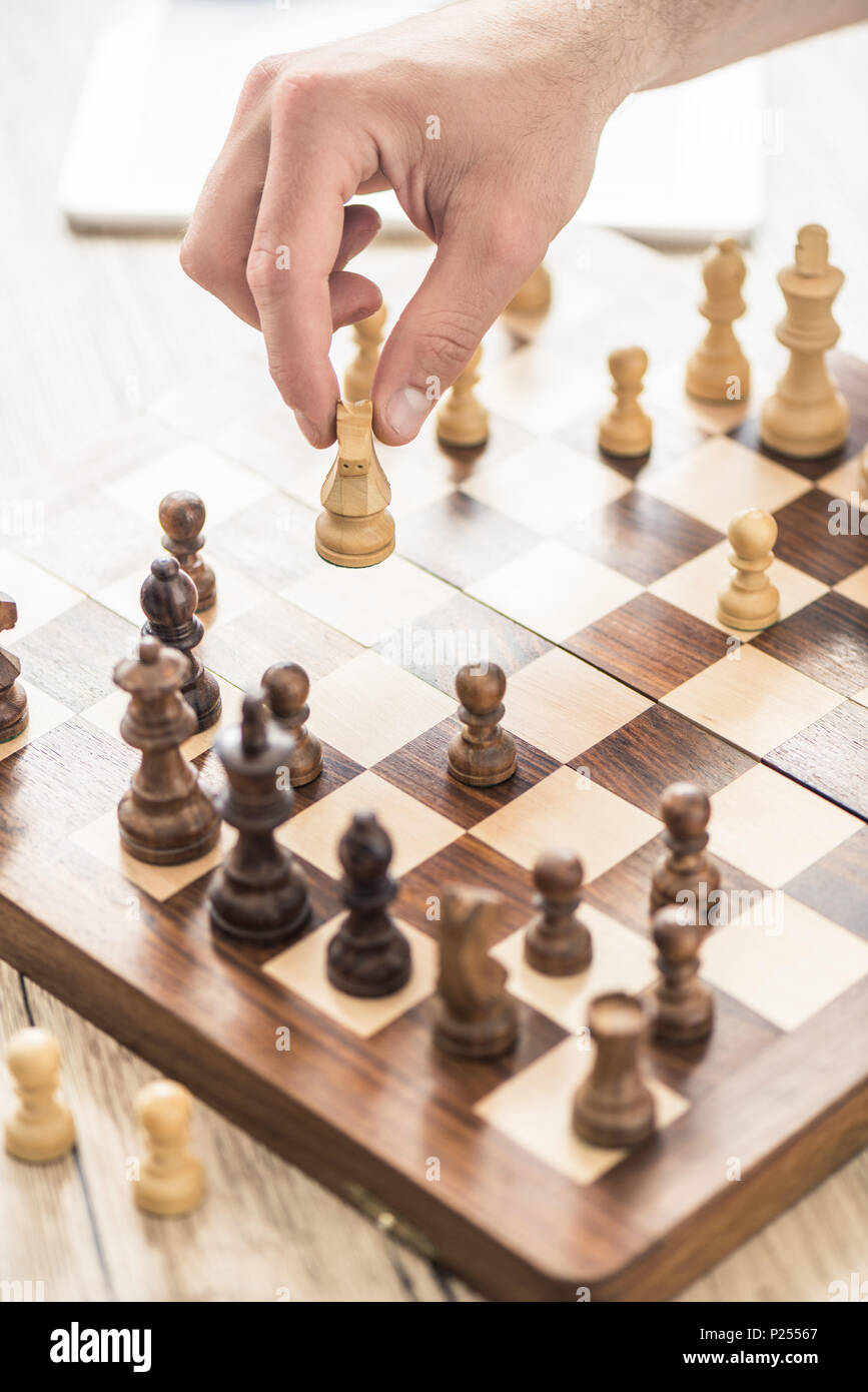 close-up partial view of person playing chess at wooden table Stock Photo